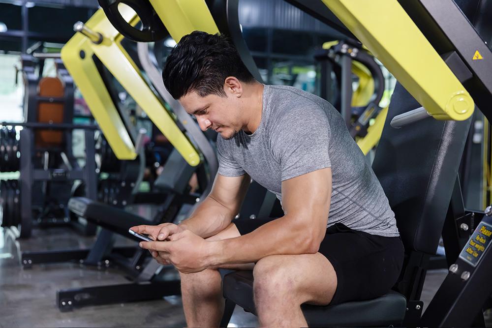 Member-sitting-on-a-machine-at-the-club-checking-his-smartphone