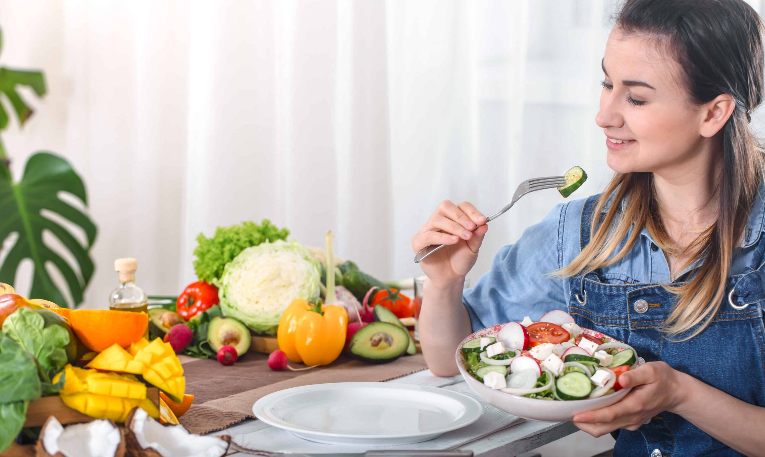 young-happy-woman-eating-salad-with-organic-vegetables-table-light-background-denim-clothes-concept-healthy-home-made-food-scaled