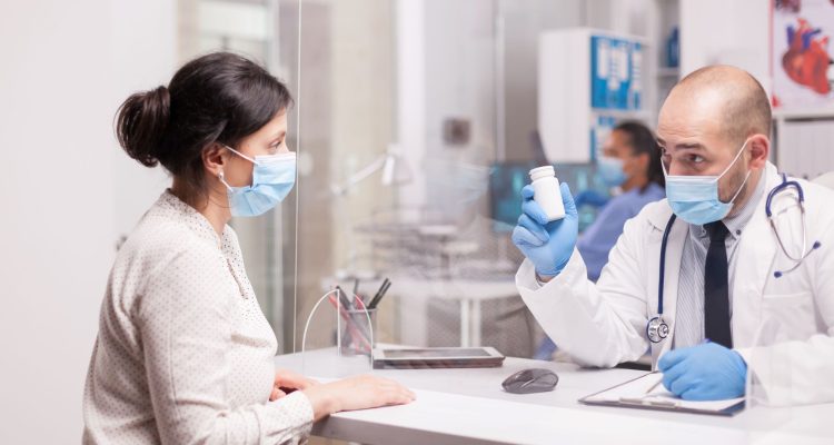 doctor-with-mask-against-coronavirus-holding-pills-bottle-patient