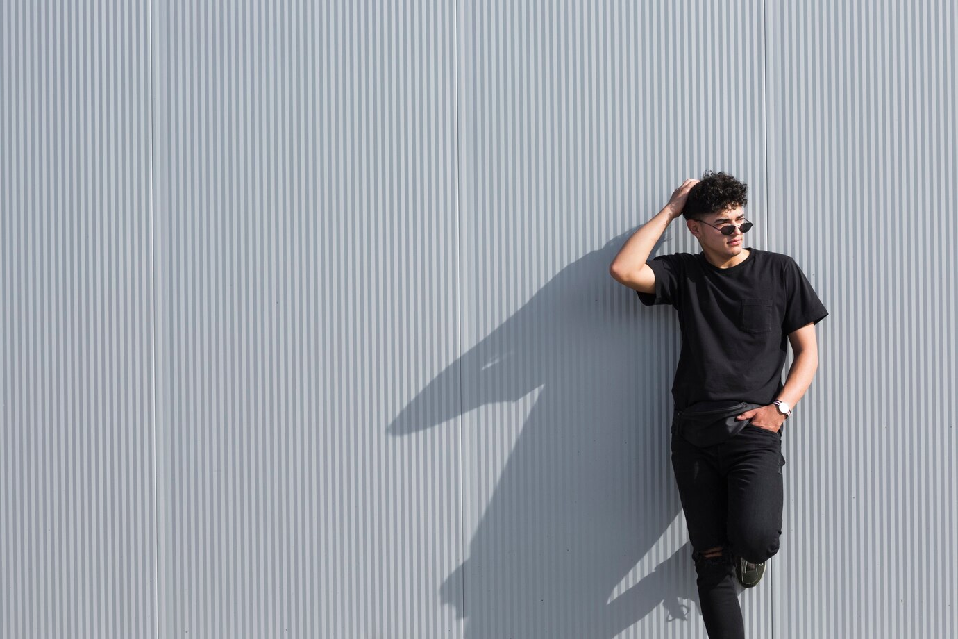 young-curly-man-sunglasses-black-clothes-leaning-grey-wall_23-2148205490