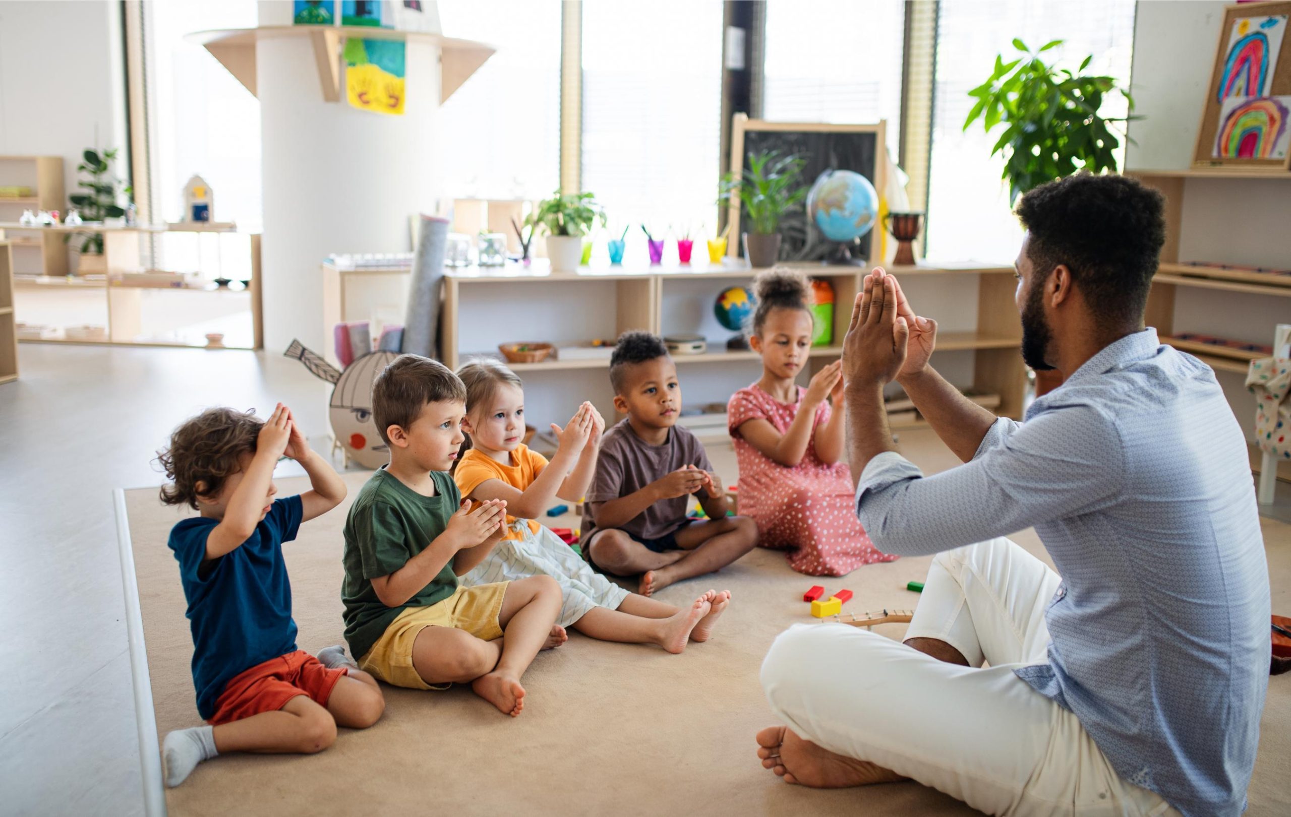 group-small-nursery-school-children-with-man-teacher-sitting-floor-indoors-classroom-playing