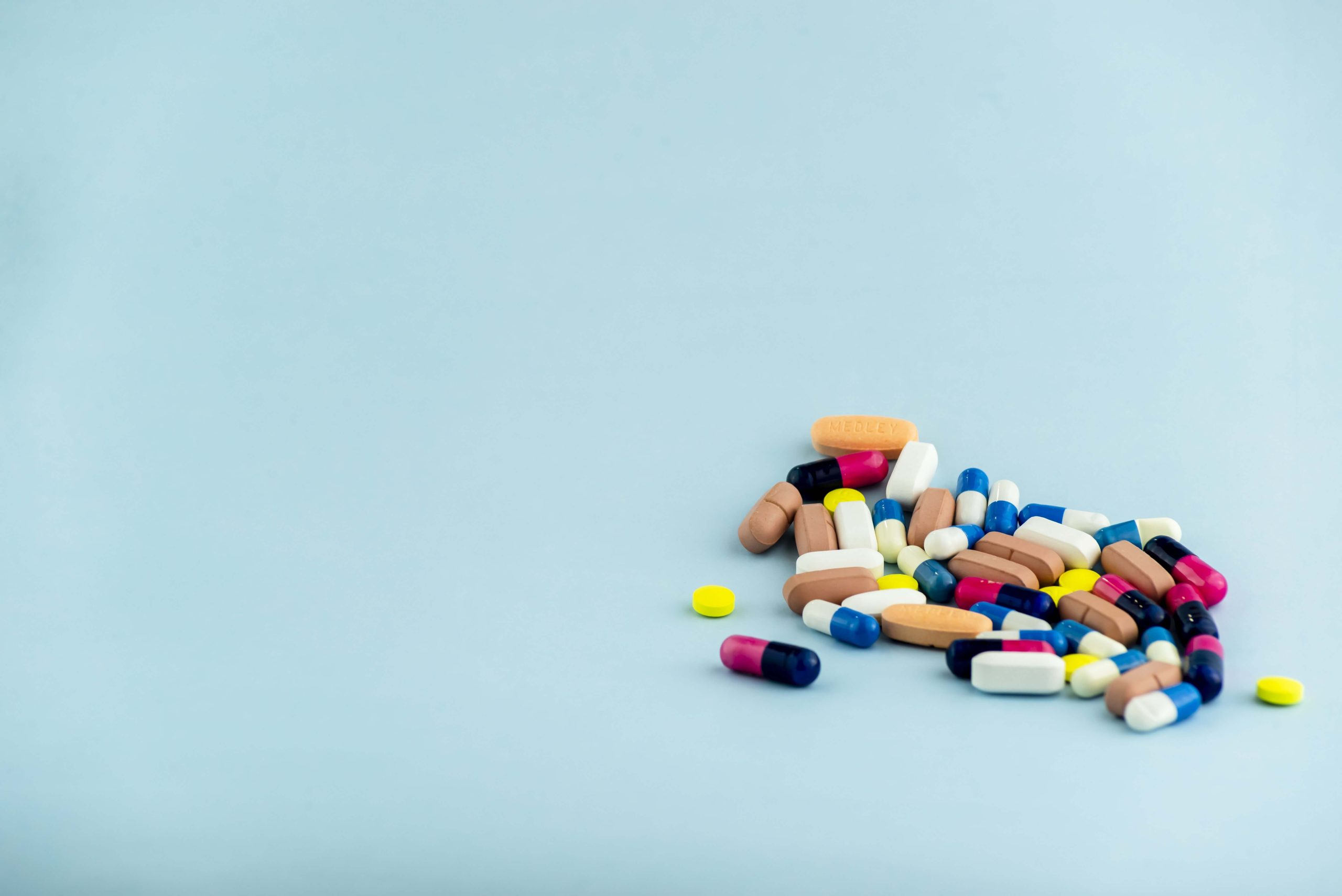 simple-pile-colorful-pills-medicines-pills-stacked-blue-background-medical-supplies-min